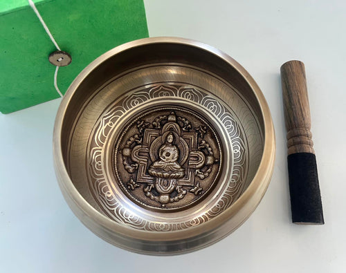 singing bowl with decorative design and wooden striking stick with buddha