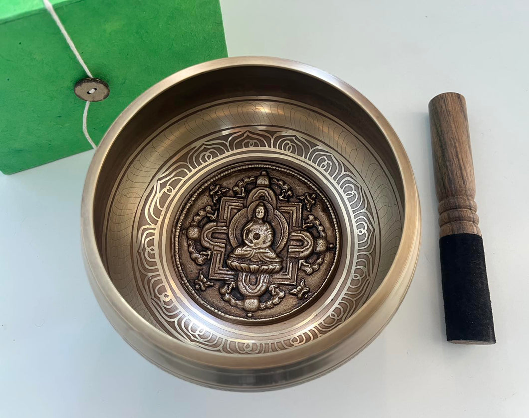 singing bowl with decorative design and wooden striking stick with buddha