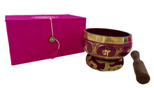 Load image into Gallery viewer, Tibetan singing bowl with gold patterns on a white surface next to a pink box.
